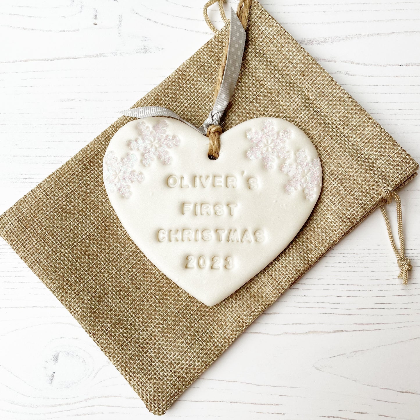 Personalised baby's first Christmas heart ornament, pearlised white clay with OLIVER’S FIRST CHRISTMAS 2023 (text not painted), decorated with 2 iridescent glitter snowflakes on either side of the top of the heart