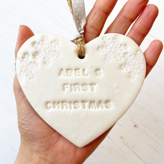 Personalised baby's first Christmas heart ornament, pearlised white clay with ABEL’S FIRST CHRISTMAS  (text not painted), decorated with 2 iridescent glitter snowflakes on either side of the top of the heart