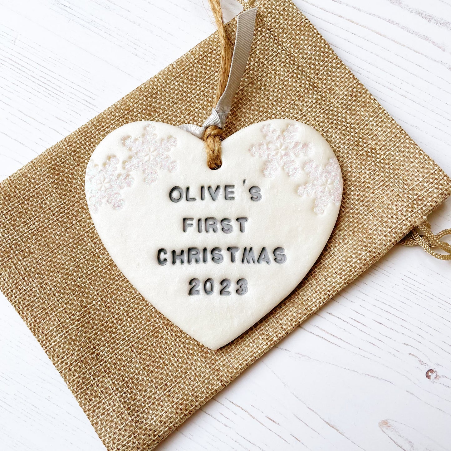 Personalised baby's first Christmas heart ornament, pearlised white clay with OLIVE'S FIRST CHRISTMAS 2023 painted grey, decorated with 2 iridescent glitter snowflakes on either side of the top of the heart