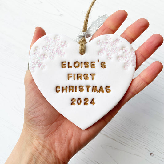 Personalised baby’s first Christmas heart ornament, glitter white clay with ELOISE’S FIRST CHRISTMAS 2024 painted gold, decorated with 2 iridescent glitter snowflakes on either side of the top of the heart