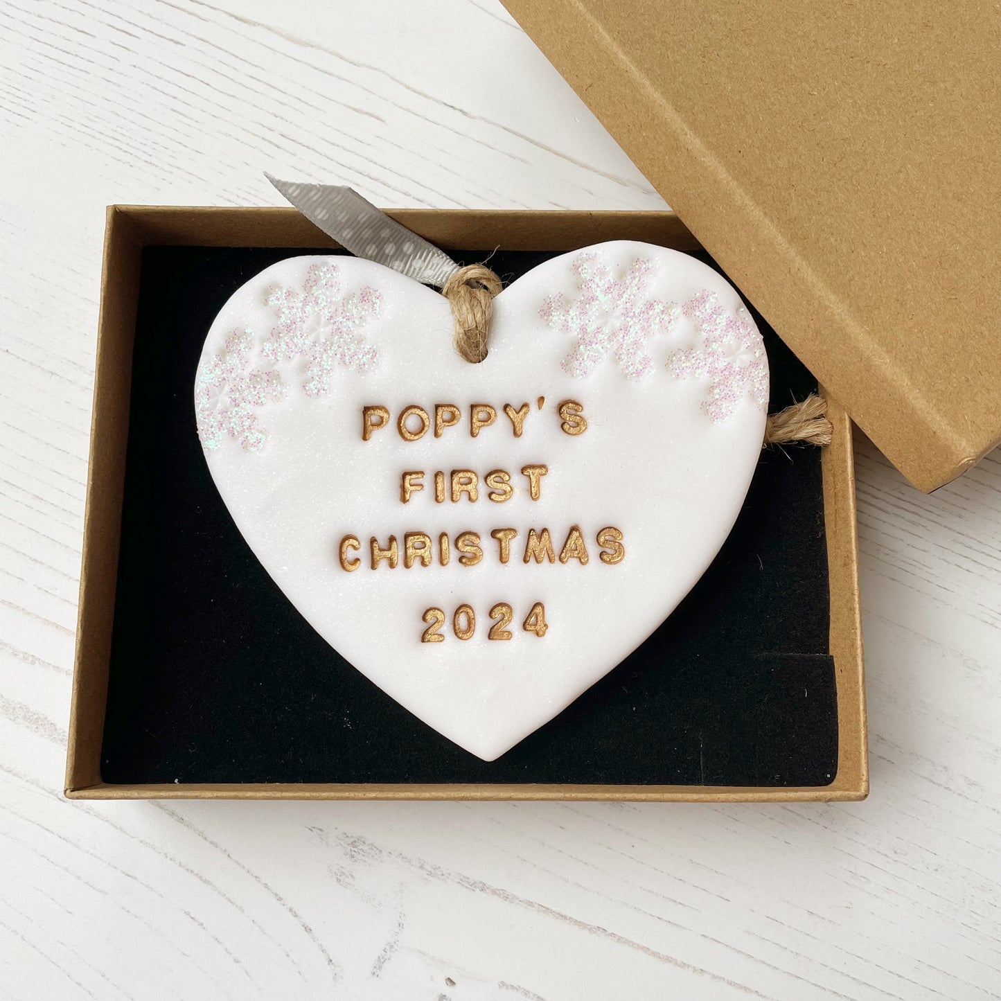 Personalised baby’s first Christmas heart ornament, glitter white clay with POPPY’S FIRST CHRISTMAS 2024 painted gold, decorated with 2 iridescent glitter snowflakes on either side of the top of the heart