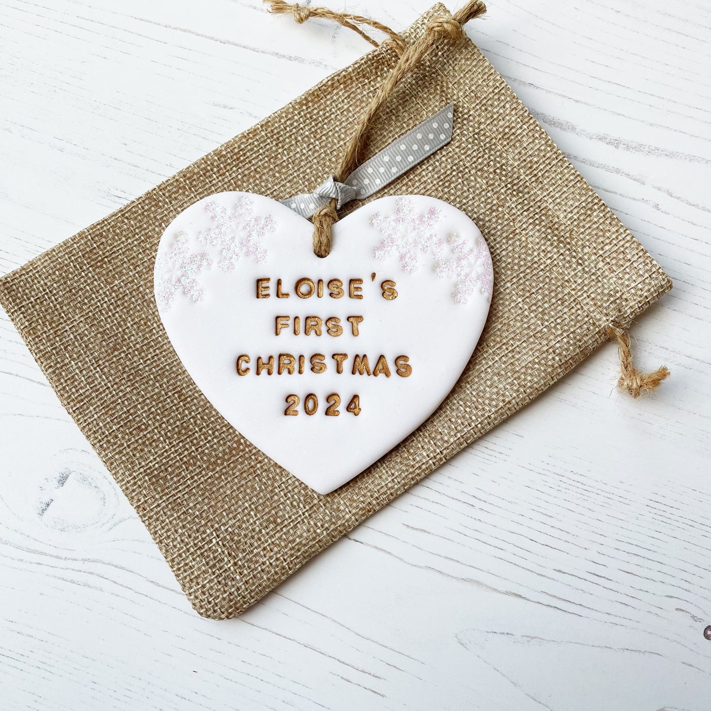 Personalised baby’s first Christmas heart ornament, glitter white clay with ELOISE’S FIRST CHRISTMAS 2024 painted gold, decorated with 2 iridescent glitter snowflakes on either side of the top of the heart