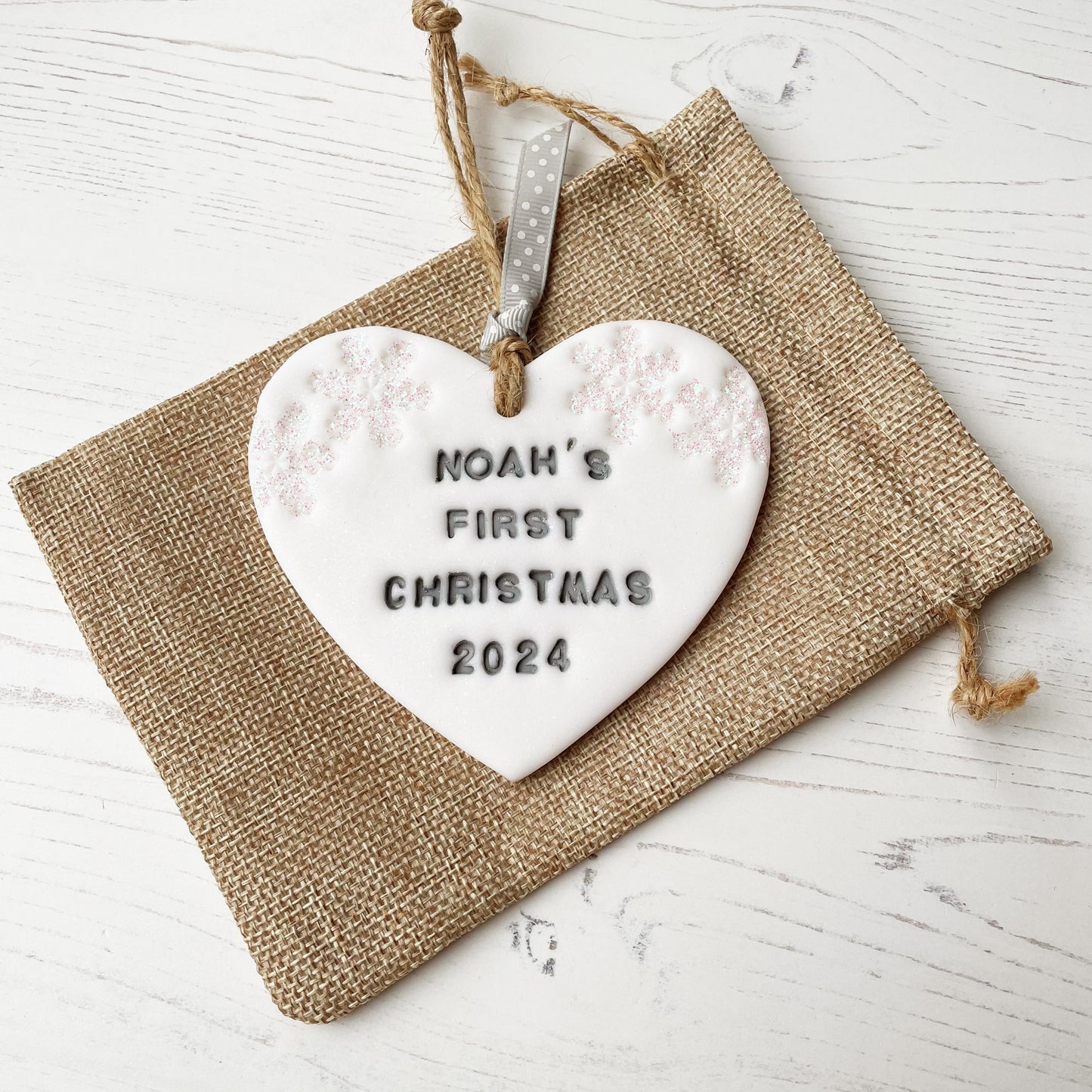 Personalised baby’s first Christmas heart ornament, glitter white clay with NOAH’S FIRST CHRISTMAS 2024 painted grey, decorated with 2 iridescent glitter snowflakes on either side of the top of the heart