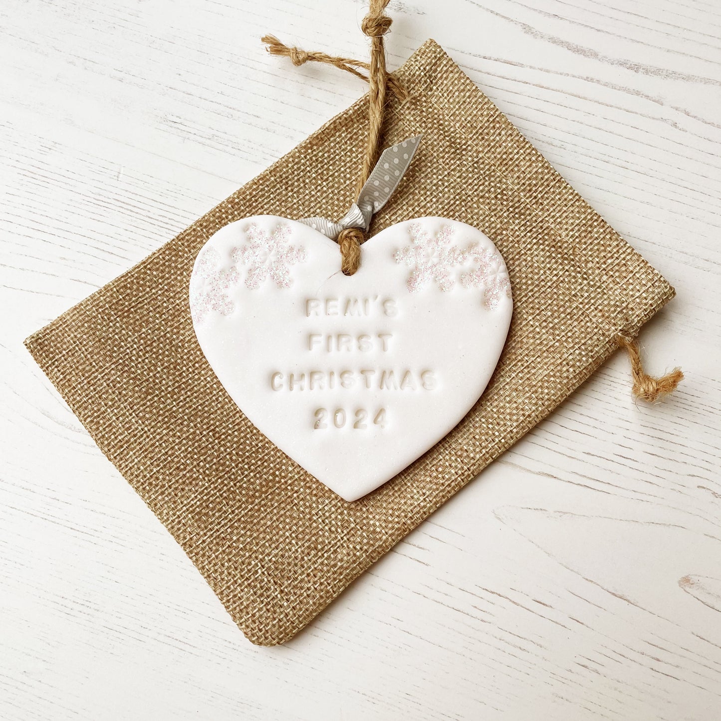 Personalised baby’s first Christmas heart ornament, glitter white clay with REMI’S FIRST CHRISTMAS 2024 (text not painted), decorated with 2 iridescent glitter snowflakes on either side of the top of the heart