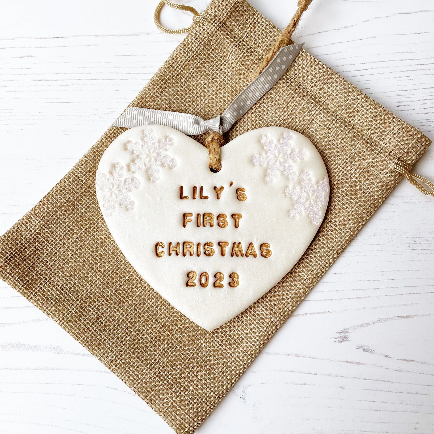 Personalised baby's first Christmas heart ornament, pearlised white clay with LILY'S FIRST CHRISTMAS 2023 painted gold, decorated with 2 iridescent glitter snowflakes on either side of the top of the heart