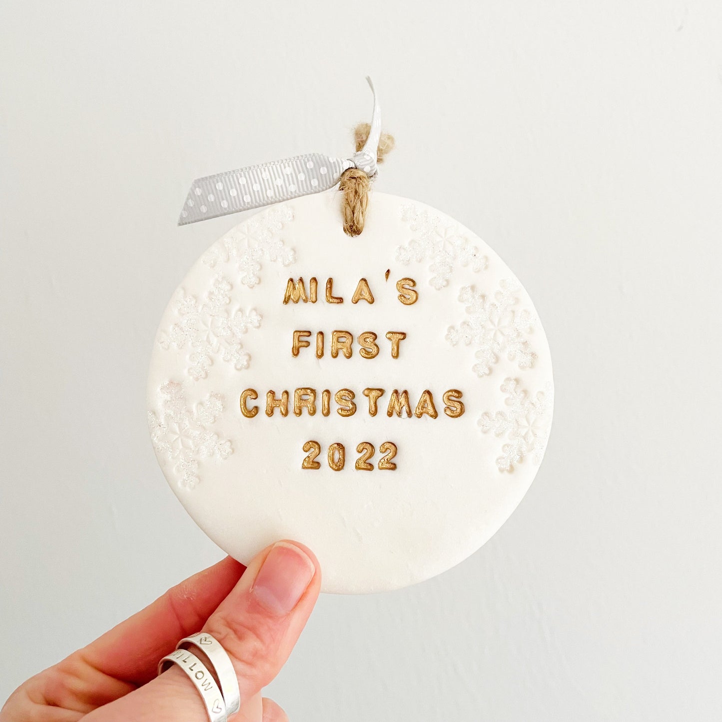 Personalised baby's first Christmas bauble ornament, pearlised white clay round personalised with Mila’s first Christmas 2022 in gold paint, decorated with 3 iridescent glitter snowflakes on either side of the bauble