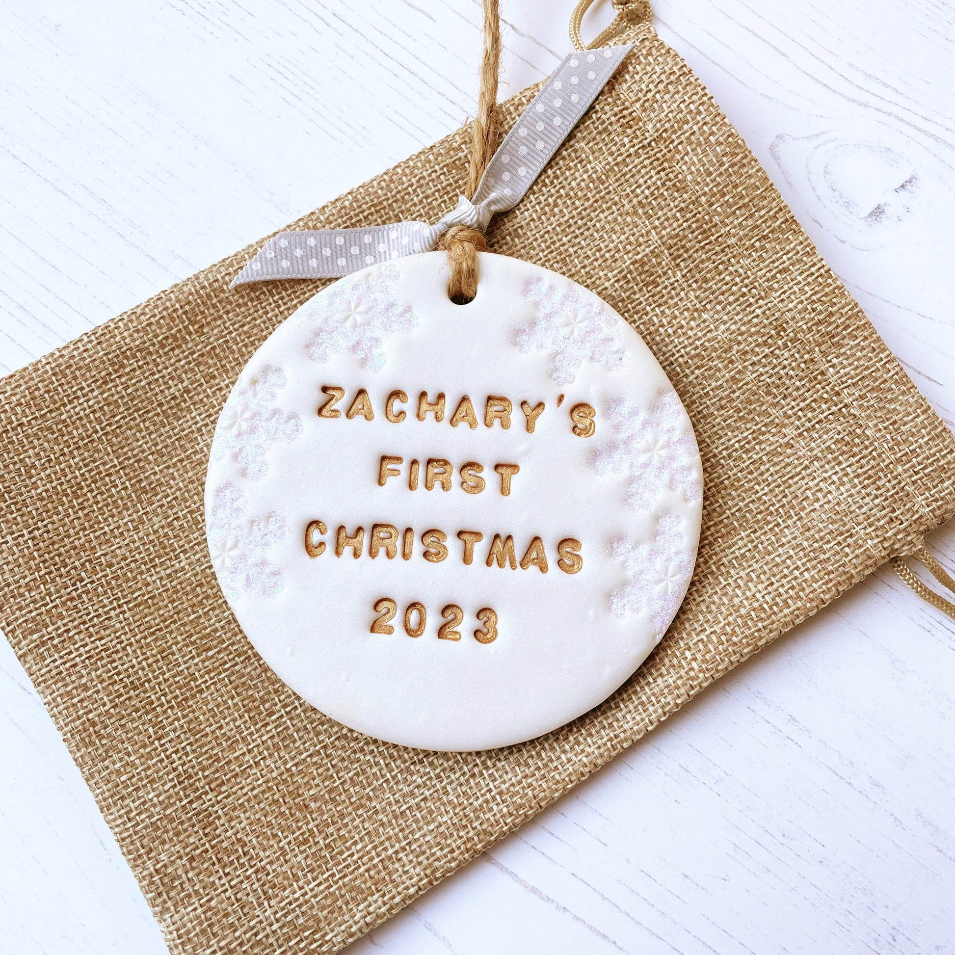 Personalised baby's first Christmas bauble ornament, pearlised white clay round personalised with Zachary’s first Christmas 2023 in gold paint, decorated with 3 iridescent glitter snowflakes on either side of the bauble
