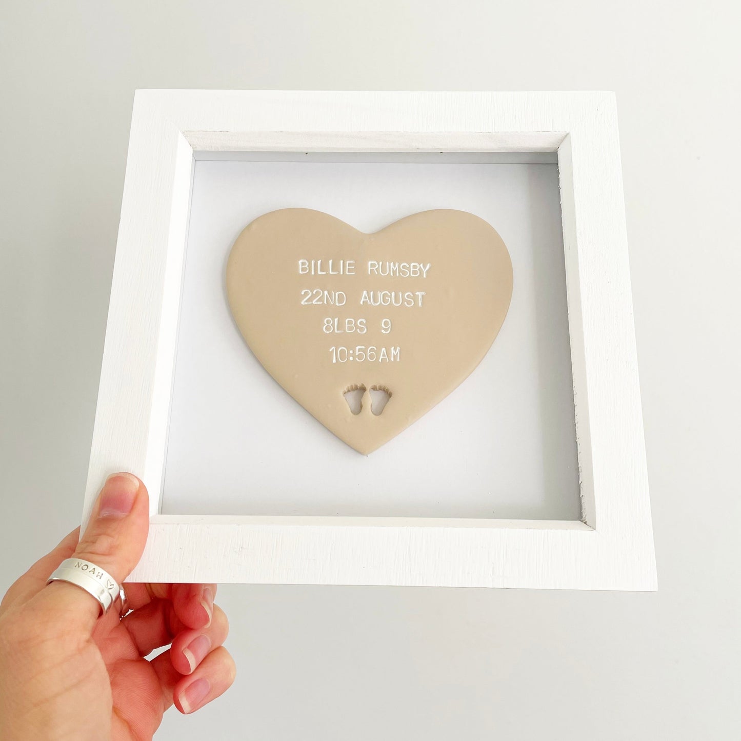 Personalised baby keepsake gift, beige clay heart with baby feet cut out at the bottom of the heart in a white box frame, the heart is personalised with the baby’s name, date of birth, weight and time