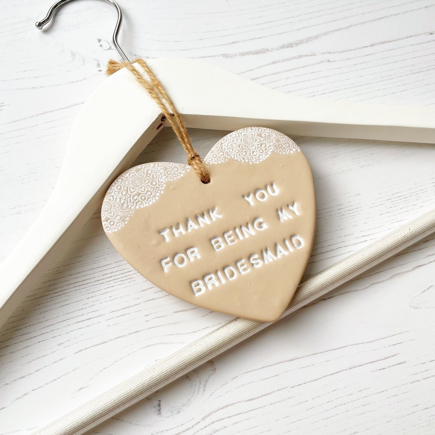 Personalised Bridesmaid thank you gift, beige clay hanging heart with a white lace edge at the top of the heart, hanging off a white coat hanger, the heart is personalised with THANK YOU FOR BEING MY BRIDESMAID