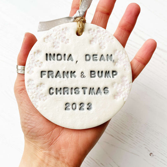 Personalised bump’s first Christmas bauble ornament, pearlised white round clay with INDIA, DEAN, FRANK & BUMP CHRISTMAS 2023 in grey paint, decorated with 3 iridescent glitter snowflakes on either side of the bauble