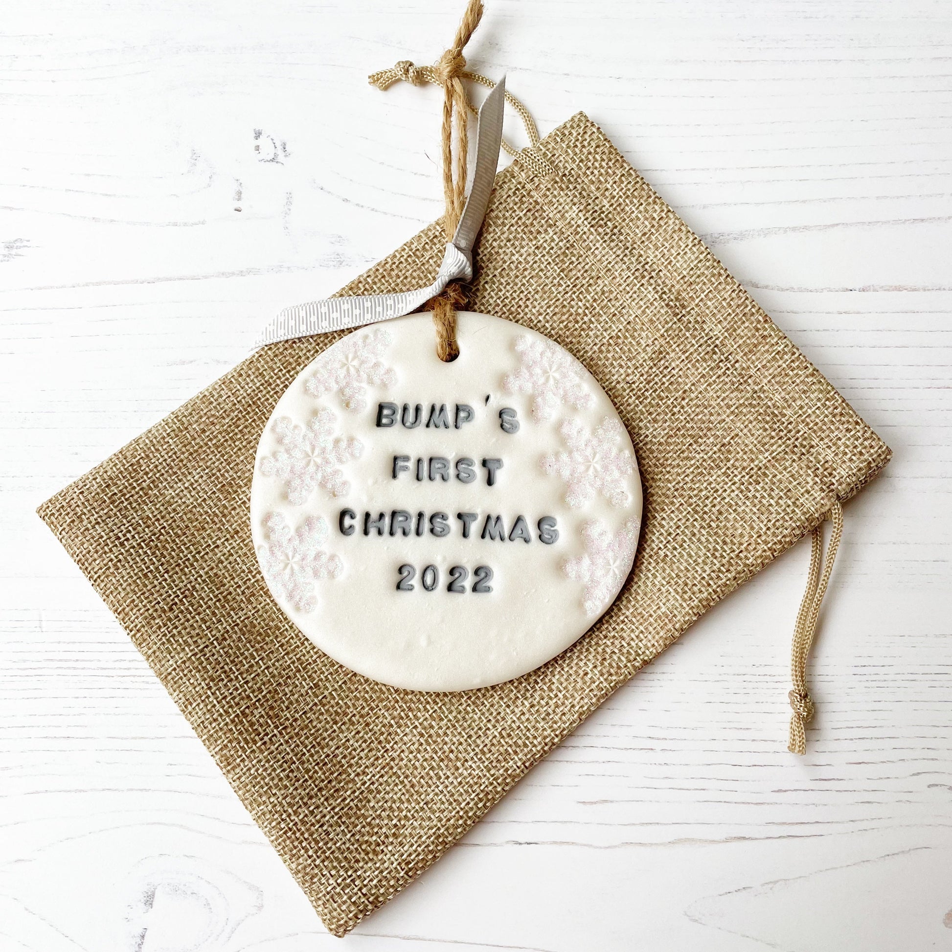 Personalised bump's first Christmas bauble ornament, pearlised white round clay with BUMP’S FIRST CHRISTMAS 2022 in grey paint, decorated with 3 iridescent glitter snowflakes on either side of the bauble