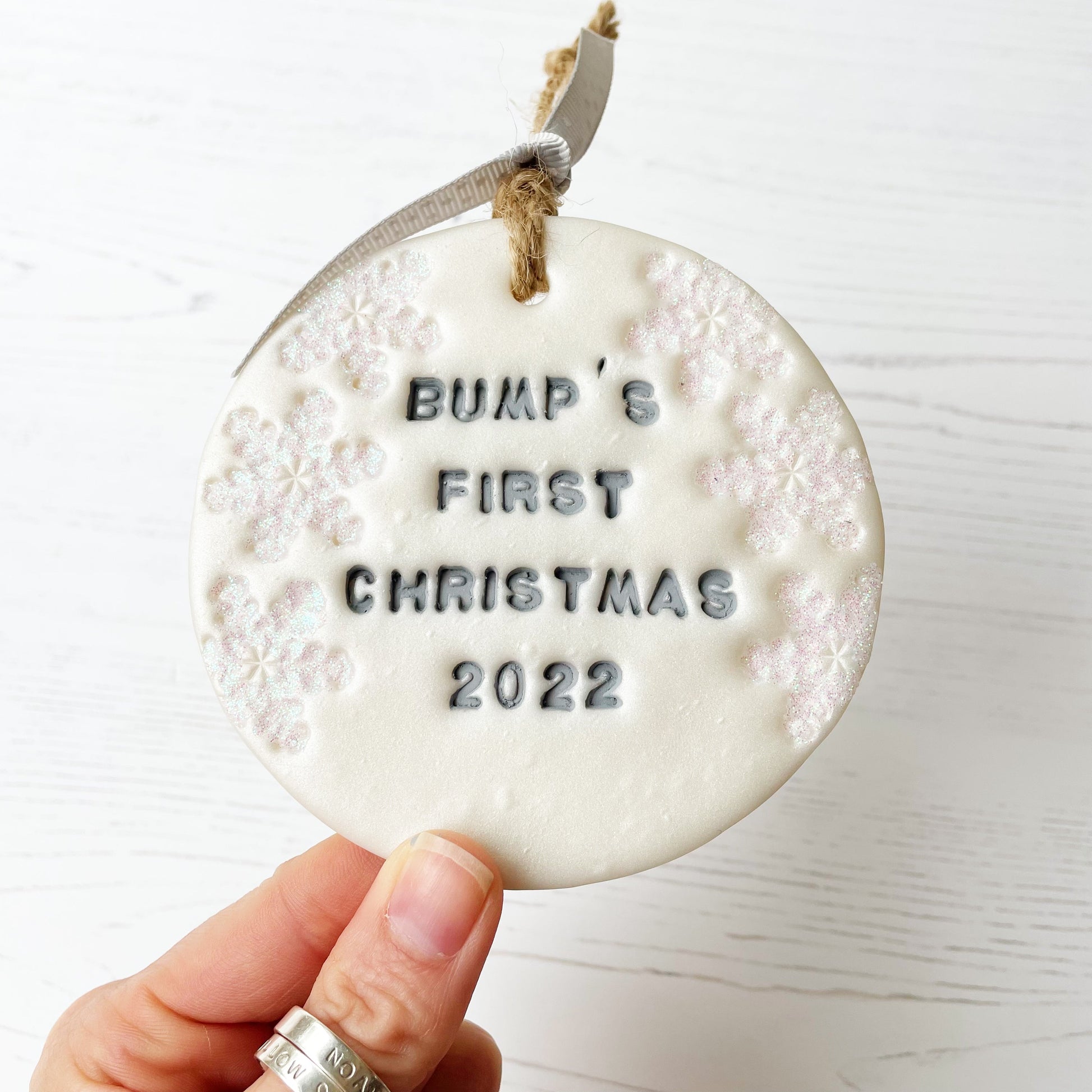 Personalised baby's first Christmas bauble ornament, pearlised white round clay with BUMP’S FIRST CHRISTMAS 2022 in grey paint, decorated with 3 iridescent glitter snowflakes on either side of the bauble