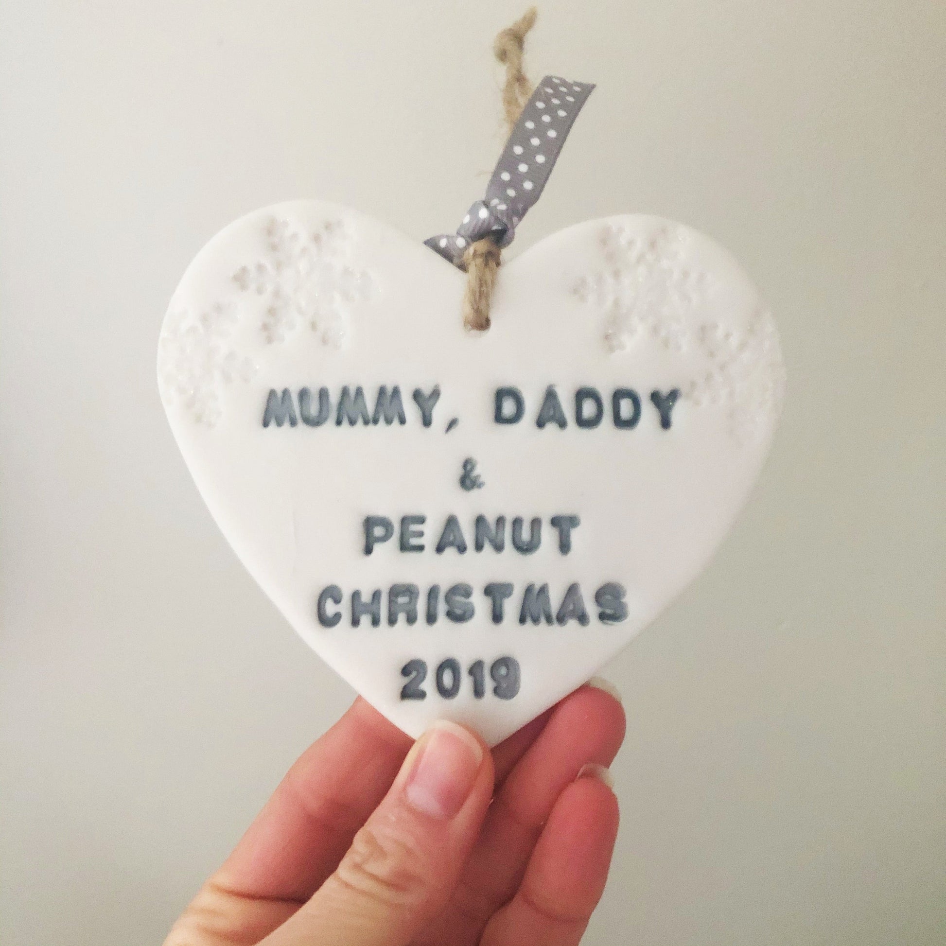 Personalised baby's first Christmas heart ornament, pearlised white clay with MUMMY, DADDY & PEANUT CHRISTMAS 2019 painted grey, decorated with 2 iridescent glitter snowflakes on either side of the top of the heart