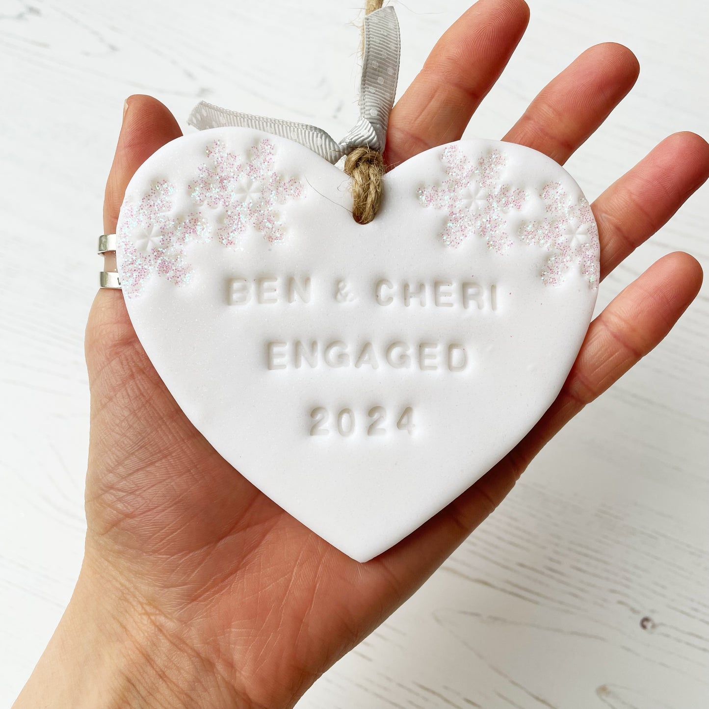 Personalised first Christmas engaged heart ornament, glitter white clay with BEN & CHERI ENGAGED 2024 (text not painted), decorated with 2 iridescent glitter snowflakes on either side of the top of the heart