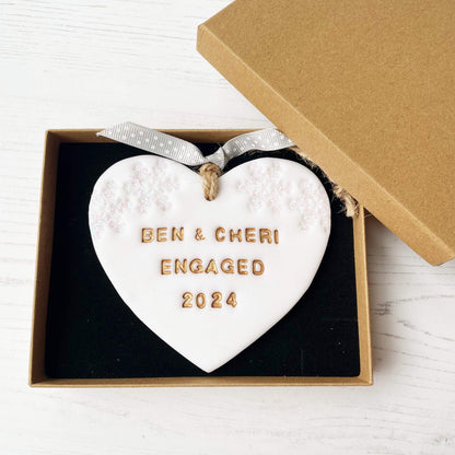 Personalised first Christmas engaged heart ornament, glitter white clay with BEN & CHERI ENGAGED 2024 painted gold, decorated with 2 iridescent glitter snowflakes on either side of the top of the heart