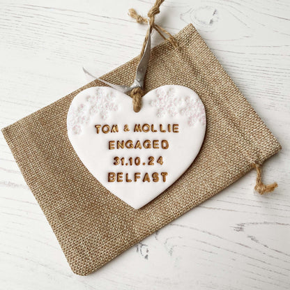 Personalised first Christmas engaged heart ornament, glitter white clay with TOM & MOLLIE ENGAGED 31.10.24 BELFAST painted gold, decorated with 2 iridescent glitter snowflakes on either side of the top of the heart