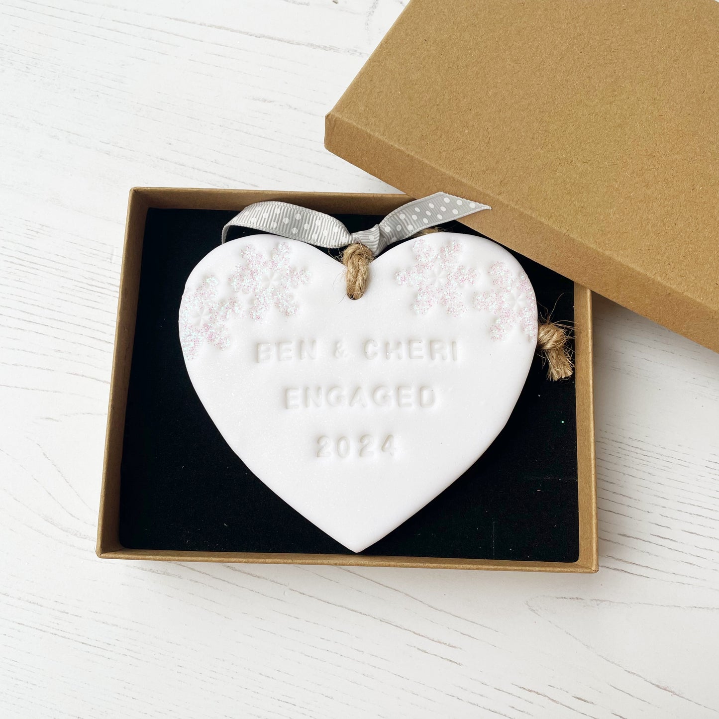 Personalised first Christmas engaged heart ornament, glitter white clay with BEN & CHERI ENGAGED 2024 (text not painted), decorated with 2 iridescent glitter snowflakes on either side of the top of the heart