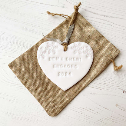 Personalised first Christmas engaged heart ornament, glitter white clay with BEN & CHERI ENGAGED 2024 (text not painted), decorated with 2 iridescent glitter snowflakes on either side of the top of the heart