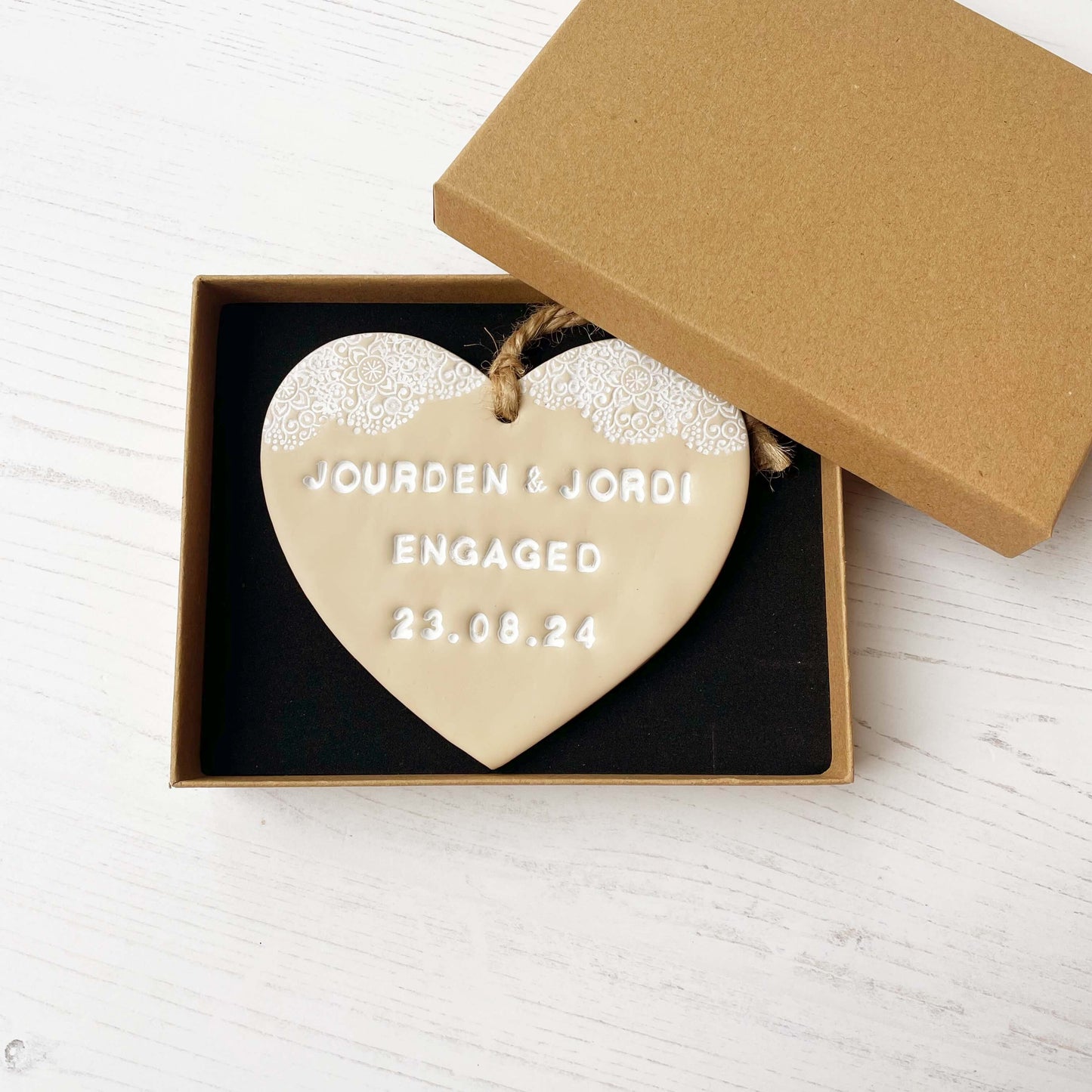 Personalised engagement gift, beige clay heart with a white lace edge at the top of the heart with jute twine for hanging, the heart is personalised with JOURDEN & JORDI ENGAGED 23.08.24