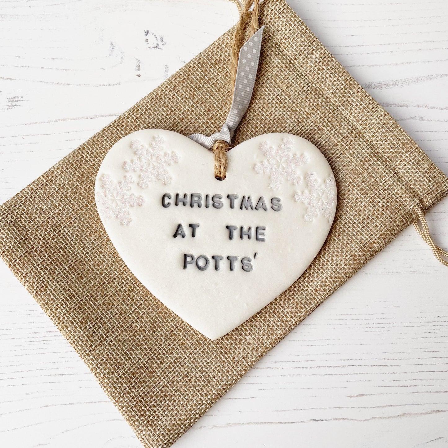 Personalised family Christmas heart ornament, pearlised white clay with CHRISTMAS AT THE POTTS’ painted grey, decorated with 2 iridescent glitter snowflakes on either side of the top of the heart