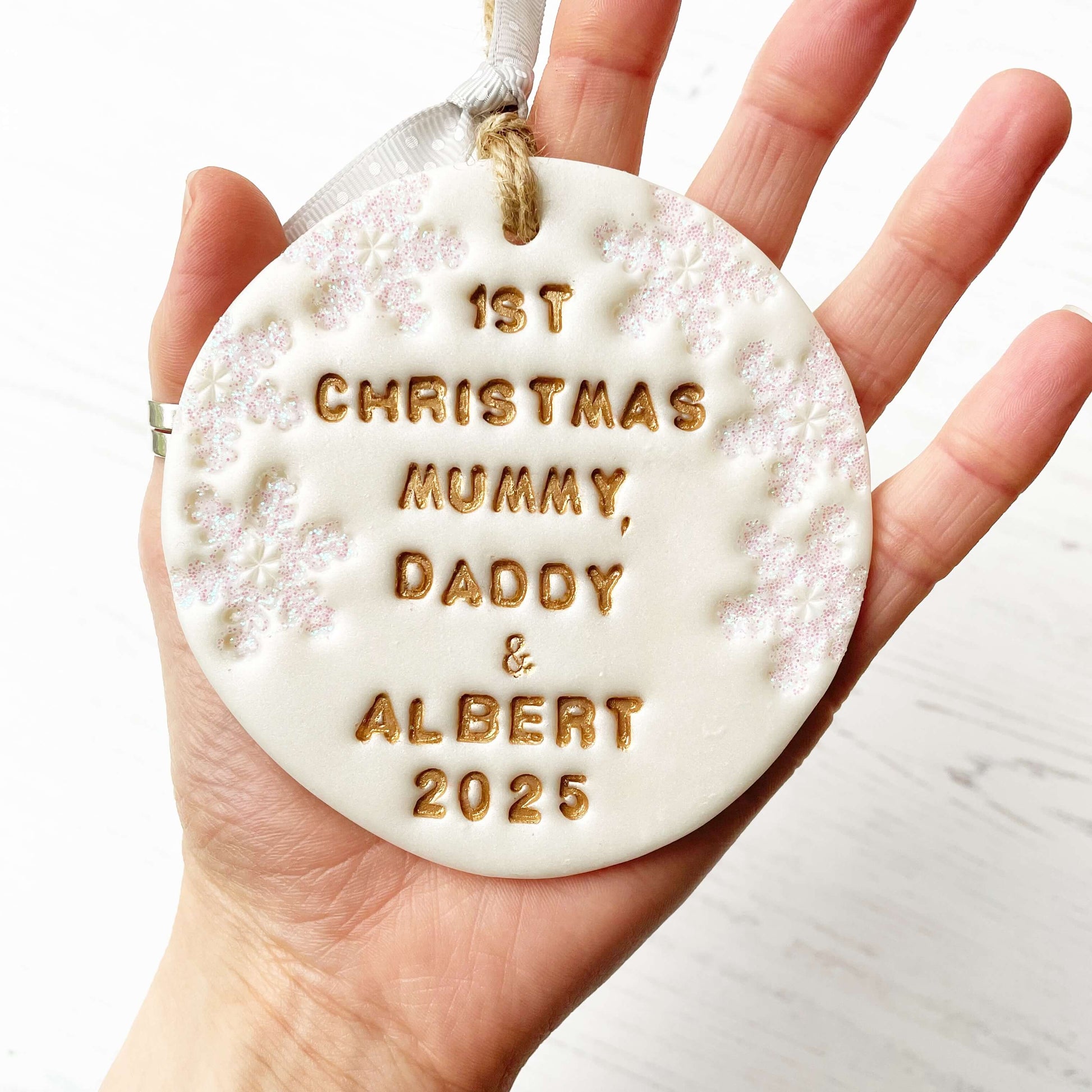 Personalised baby’s first Christmas bauble ornament, pearlised white clay round personalised with 1ST CHRISTMAS MUMMY, DADDY & ALBERT 2025 in gold paint, decorated with 3 iridescent glitter snowflakes on either side of the bauble
