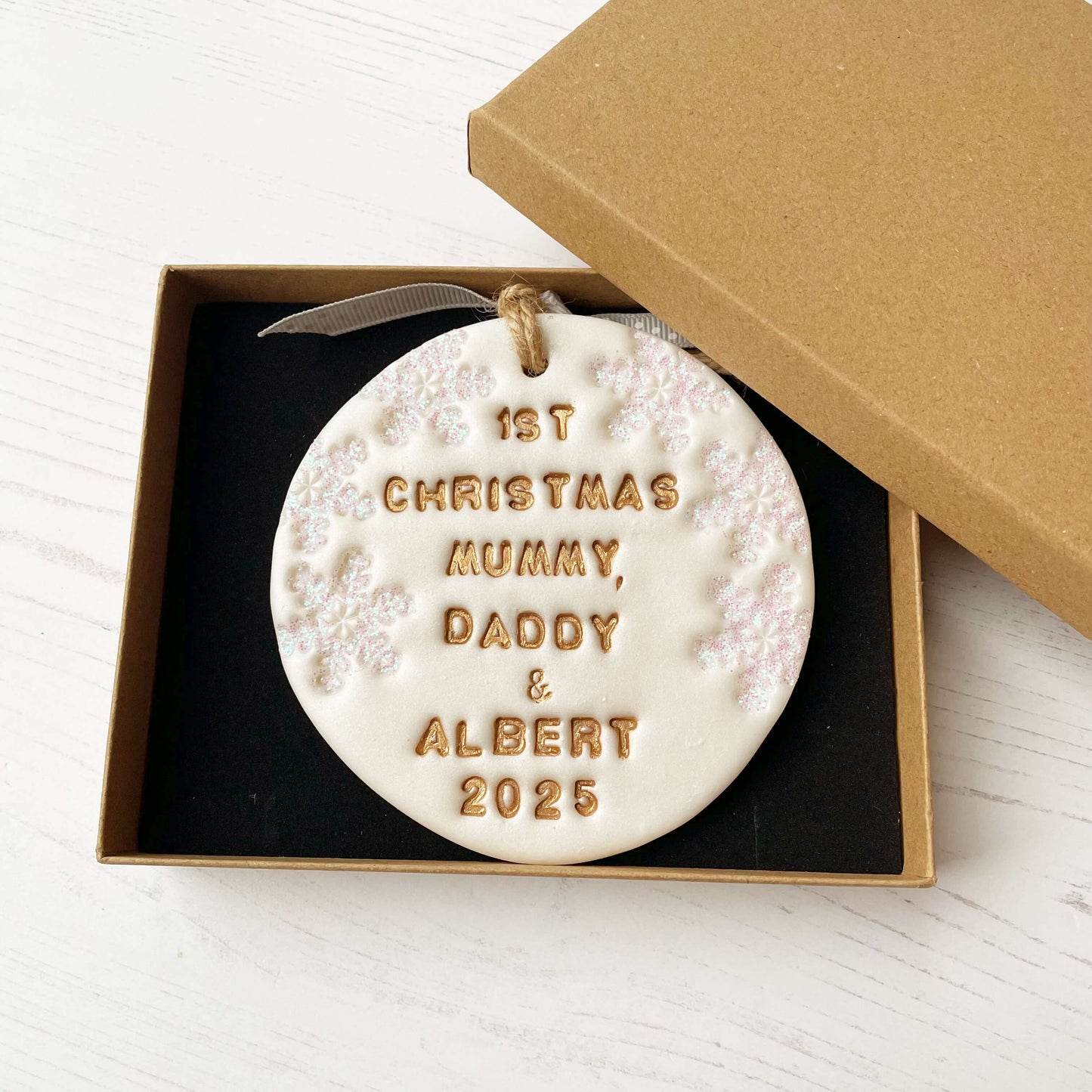 Personalised baby’s first Christmas bauble ornament, pearlised white clay round personalised with 1ST CHRISTMAS MUMMY, DADDY & ALBERT 2025 in gold paint, decorated with 3 iridescent glitter snowflakes on either side of the bauble