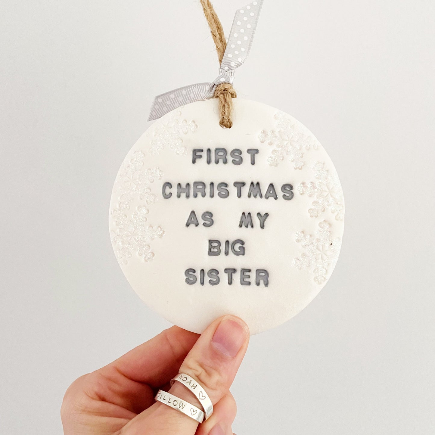 Personalised baby's first Christmas bauble ornament, pearlised white round clay with FIRST CHRISTMAS AS MY BIG SISTER in grey paint, decorated with 3 iridescent glitter snowflakes on either side of the bauble