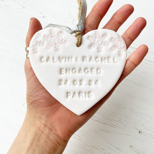 Personalised first Christmas engaged heart ornament, glitter white clay with CALVIN & RACHEL ENGAGED 24.02.24 PARIS (text not painted), decorated with 2 iridescent glitter snowflakes on either side of the top of the heart