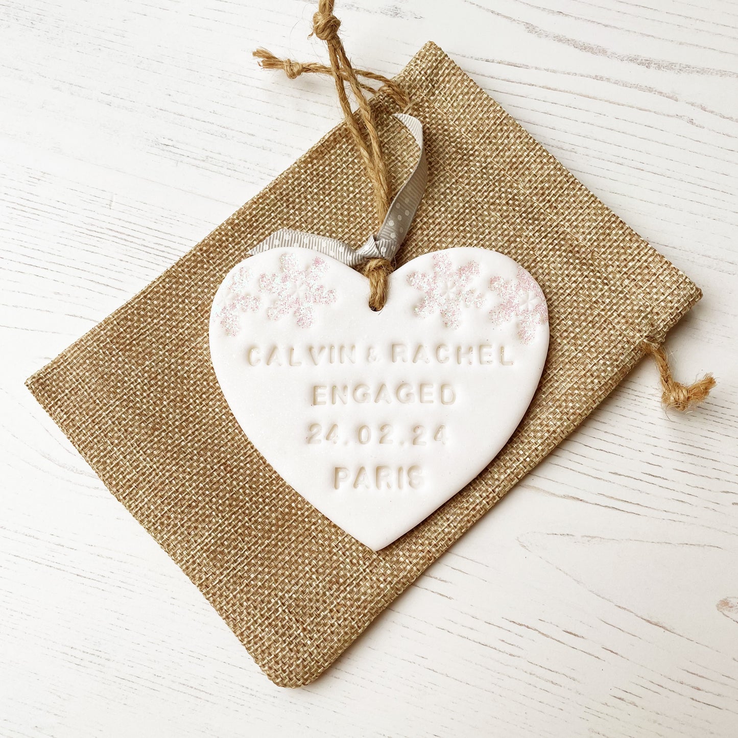 Personalised first Christmas engaged heart ornament, glitter white clay with CALVIN & RACHEL ENGAGED 24.02.24 PARIS (text not painted), decorated with 2 iridescent glitter snowflakes on either side of the top of the heart