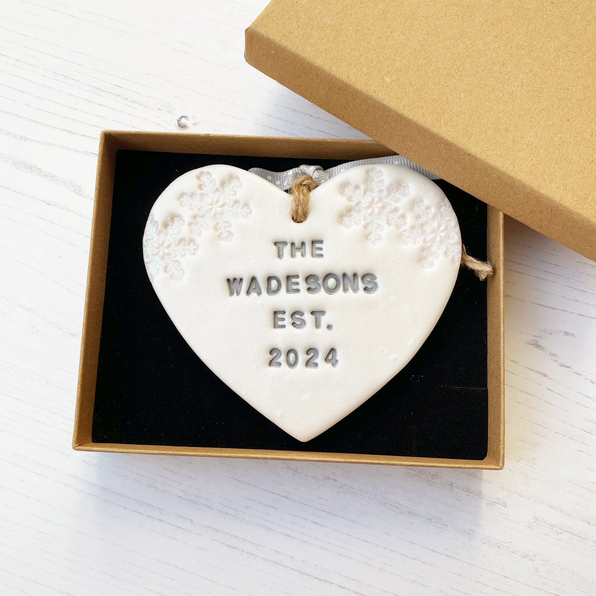 Personalised first Christmas married heart ornament, pearlised white clay personalised in grey with THE WADESONS EST. 2024, decorated with 2 iridescent glitter snowflakes on either side of the top of the heart