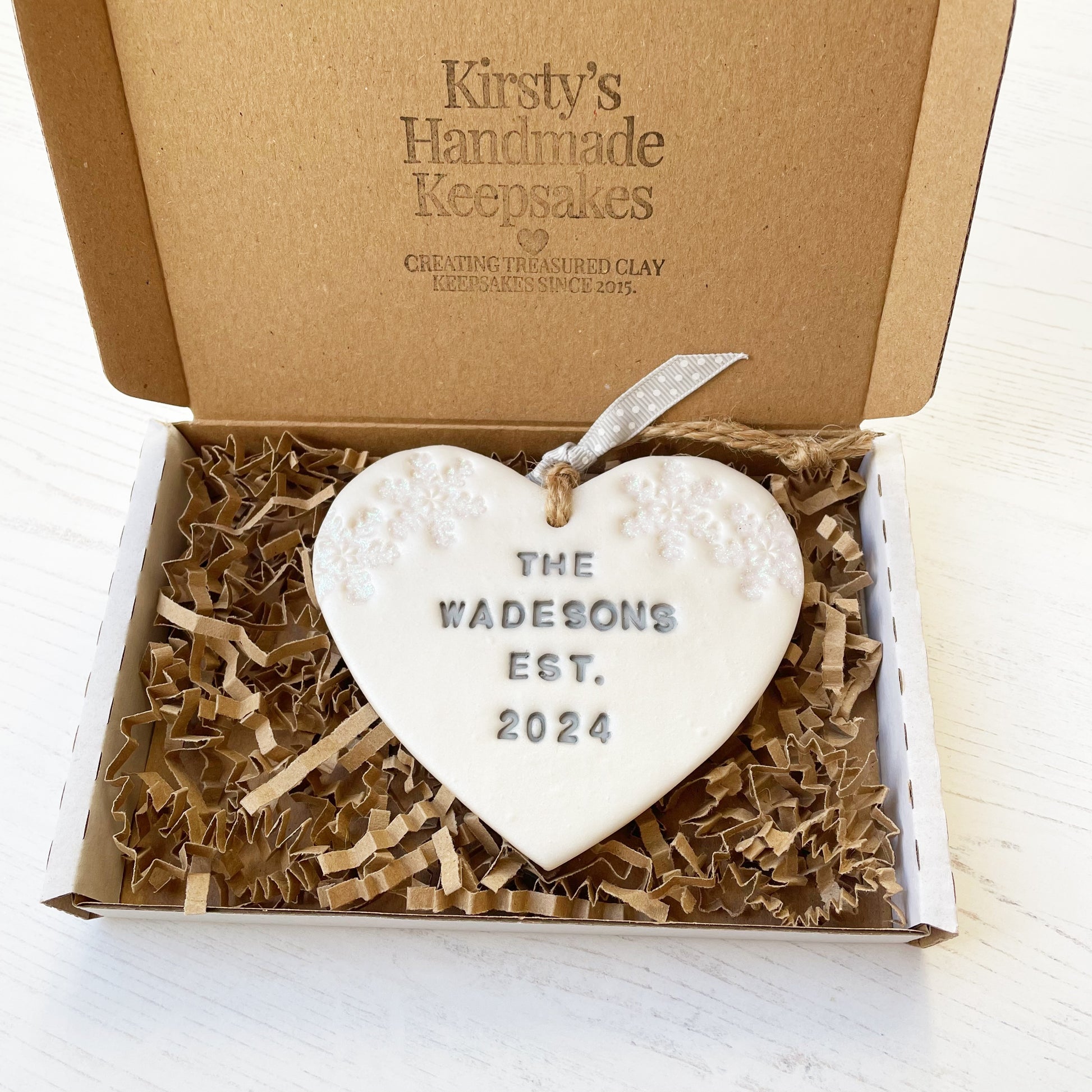 Personalised first Christmas married heart ornament, pearlised white clay personalised in grey with THE WADESONS EST. 2024, decorated with 2 iridescent glitter snowflakes on either side of the top of the heart