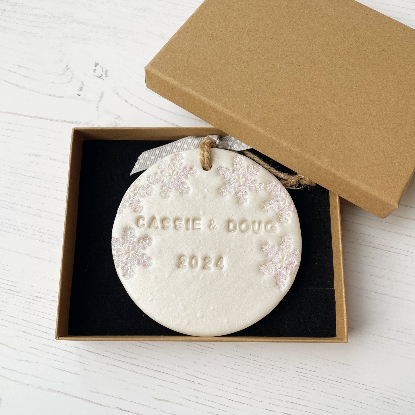 Personalised our first Christmas together bauble ornament, pearlised white round clay with CASSIE & DOUG 2024 (text not painted), decorated with 3 iridescent glitter snowflakes on either side of the bauble