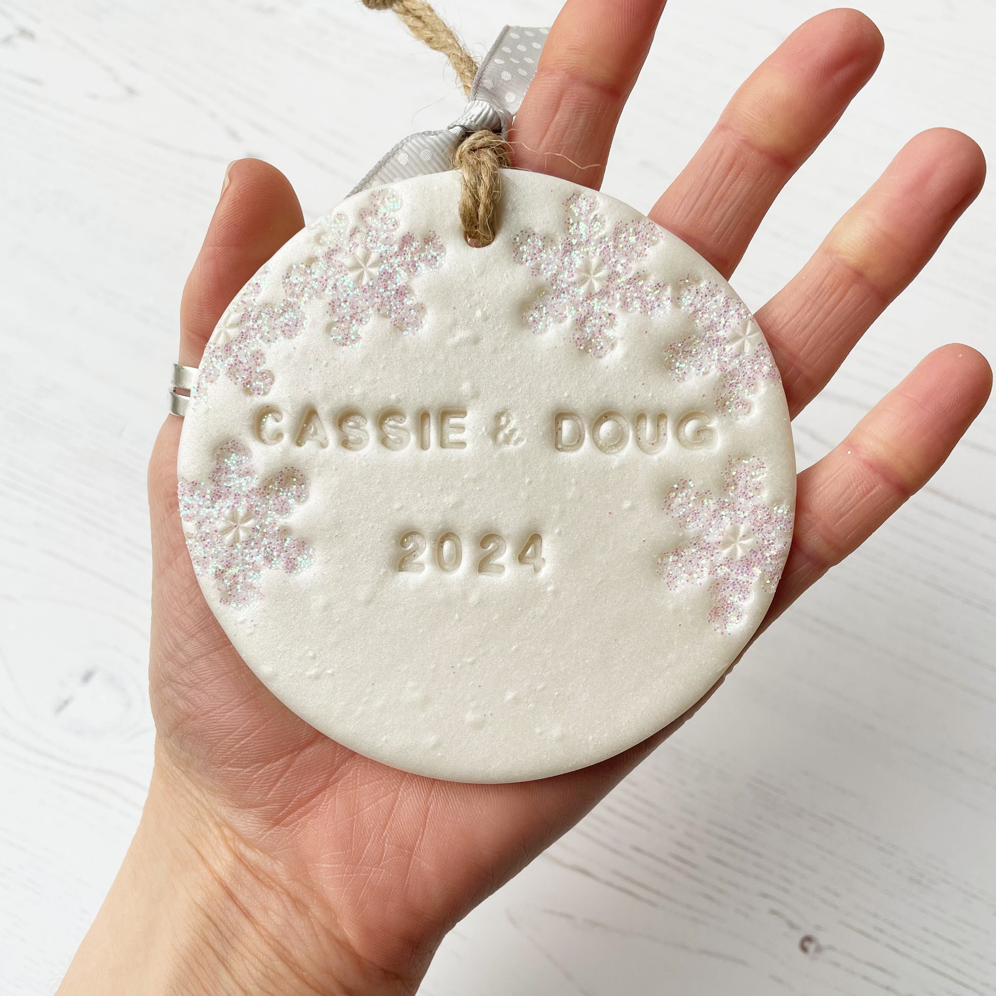 Personalised our first Christmas together bauble ornament, pearlised white round clay with CASSIE & DOUG 2024 (text not painted), decorated with 3 iridescent glitter snowflakes on either side of the bauble