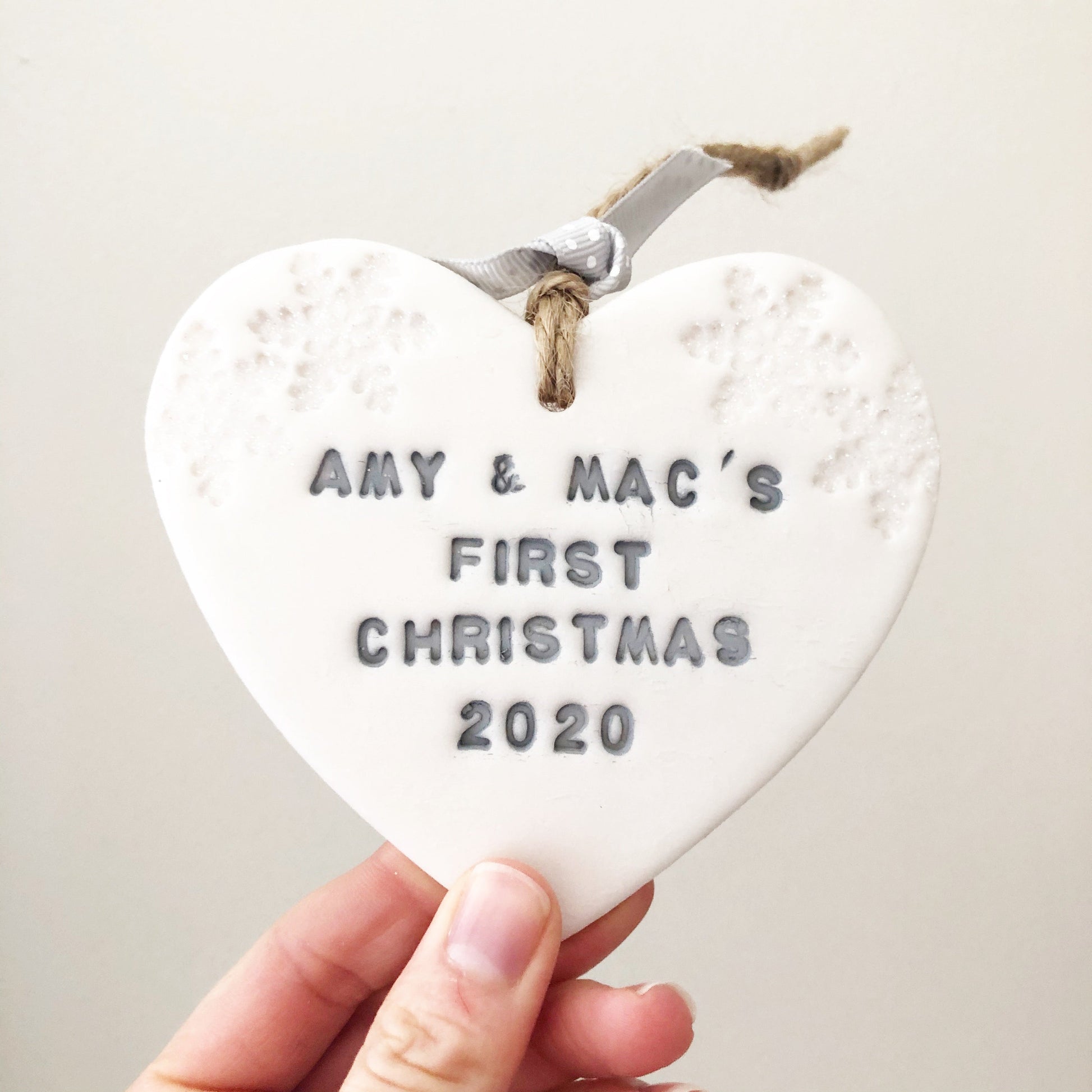 Personalised baby's first Christmas heart ornament, pearlised white clay with AMY & MAC'S FIRST CHRISTMAS 2020 painted grey, decorated with 2 iridescent glitter snowflakes on either side of the top of the heart