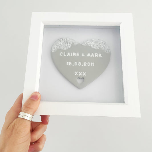 Personalised anniversary gift, grey clay heart with a white lace edge at the top of the heart and a heart cut out at the bottom in a white box frame, the heart is personalised with CLAIRE & MARK 18.08.2011 XXX