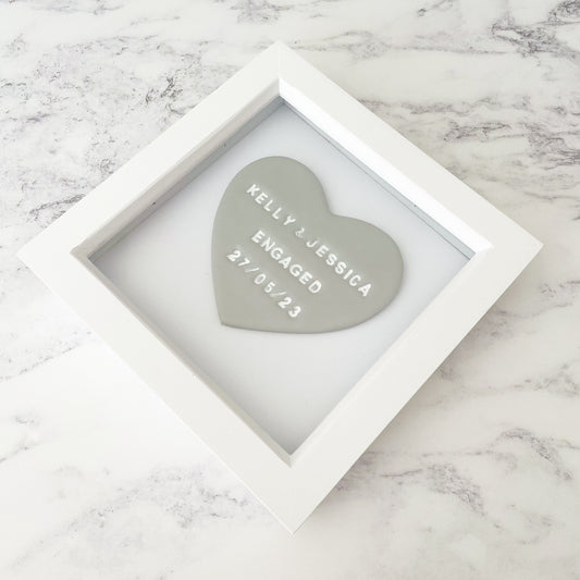 Personalised framed engagement gift, grey clay heart in a white box frame, the heart is personalised with KELLY & JESSICA ENGAGED 27/05/23