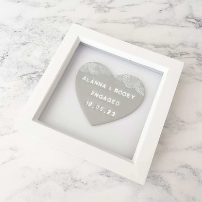 Personalised framed engagement gift, grey clay heart with a white lace edge at the top of the heart in a white box frame, the heart is personalised with ALANNA & ROOEY ENGAGED 18.05.23