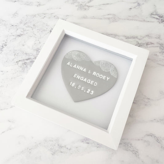 Personalised framed engagement gift, grey clay heart with a white lace edge at the top of the heart in a white box frame, the heart is personalised with ALANNA & ROOEY ENGAGED 18.05.23