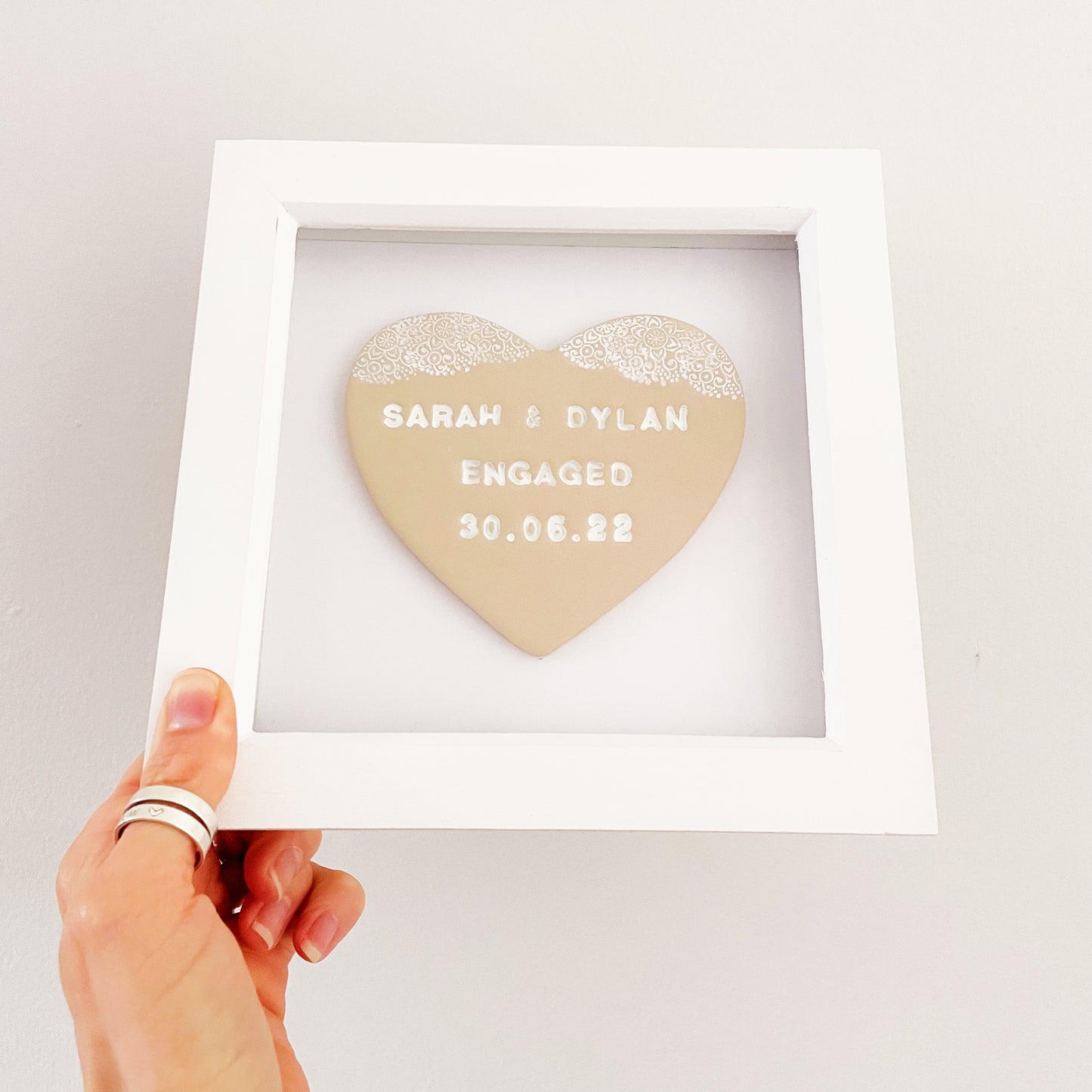 Personalised beige clay heart with a white lace edge at the top, in a white box frame, the heart is personalised with SARAH & DYLAN ENGAGED 30.06.22
