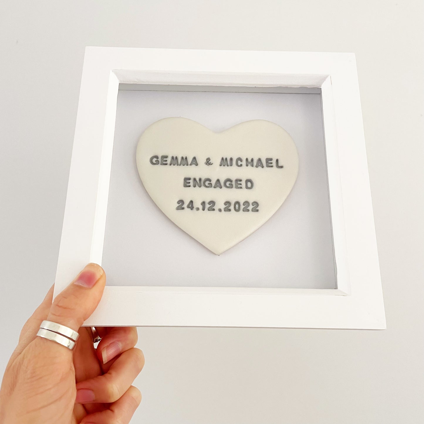 Personalised pearlised white clay heart in a white box frame, the heart is personalised with GEMMA & MICHAEL ENGAGED 24.12.2022