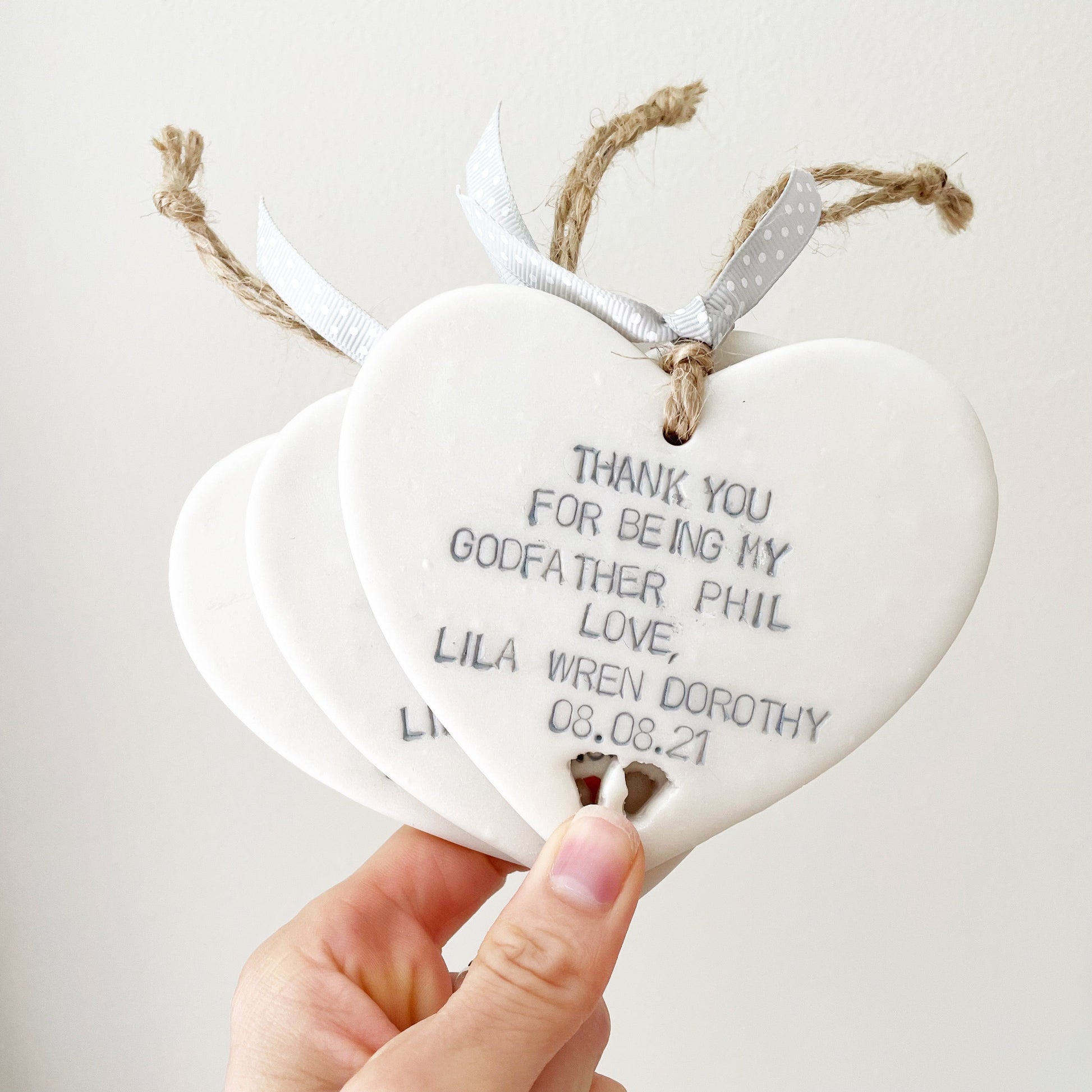 Personalised Godfather gift, 3 pearlised white clay hanging hearts with baby feet cut out of the bottom, the heart is personalised with THANK YOU FOR BEING MY GODFATHER PHIL LOVE, LILA WREN DOROTHY 08.08.21
