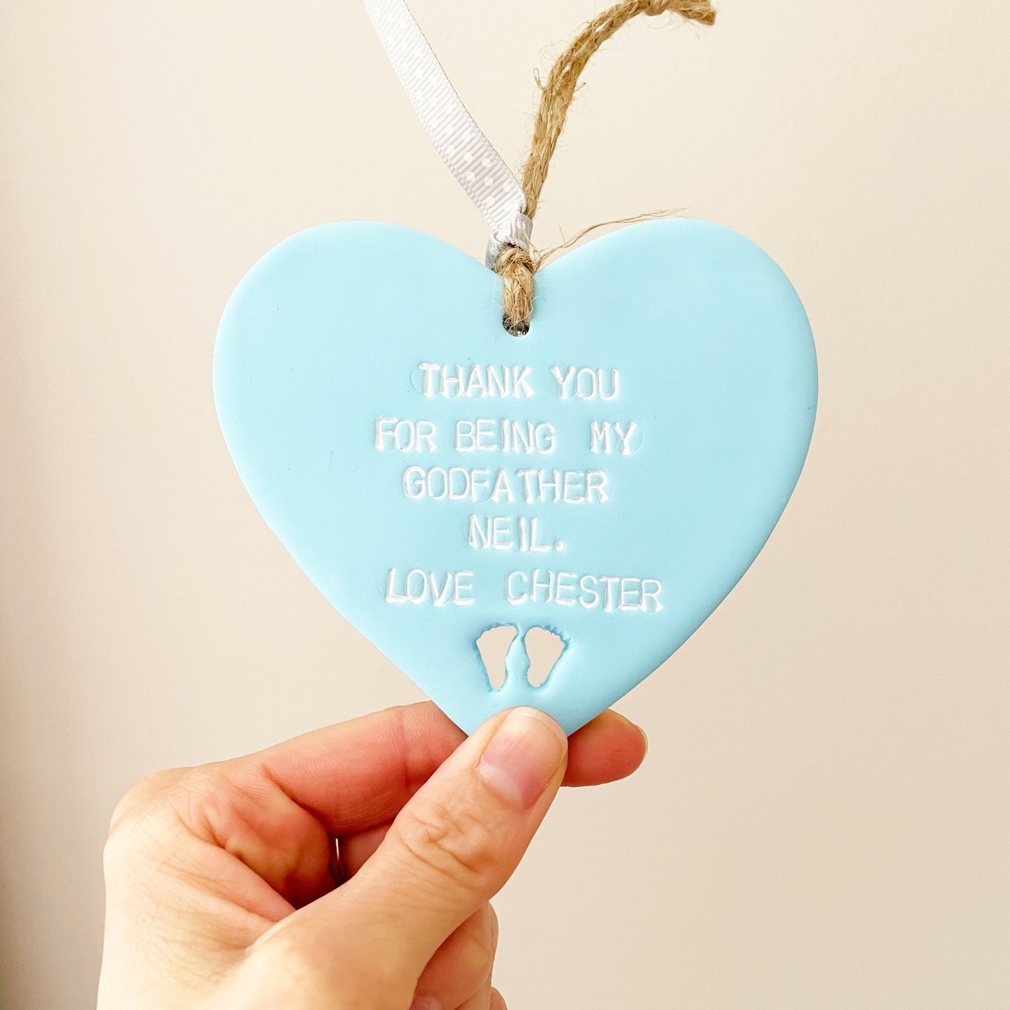 Personalised Godfather gift, pastel blue clay hanging heart with baby feet cut out of the bottom, the heart is personalised with THANK YOU FOR BEING MY GODFATHER NEIL LOVE CHESTER