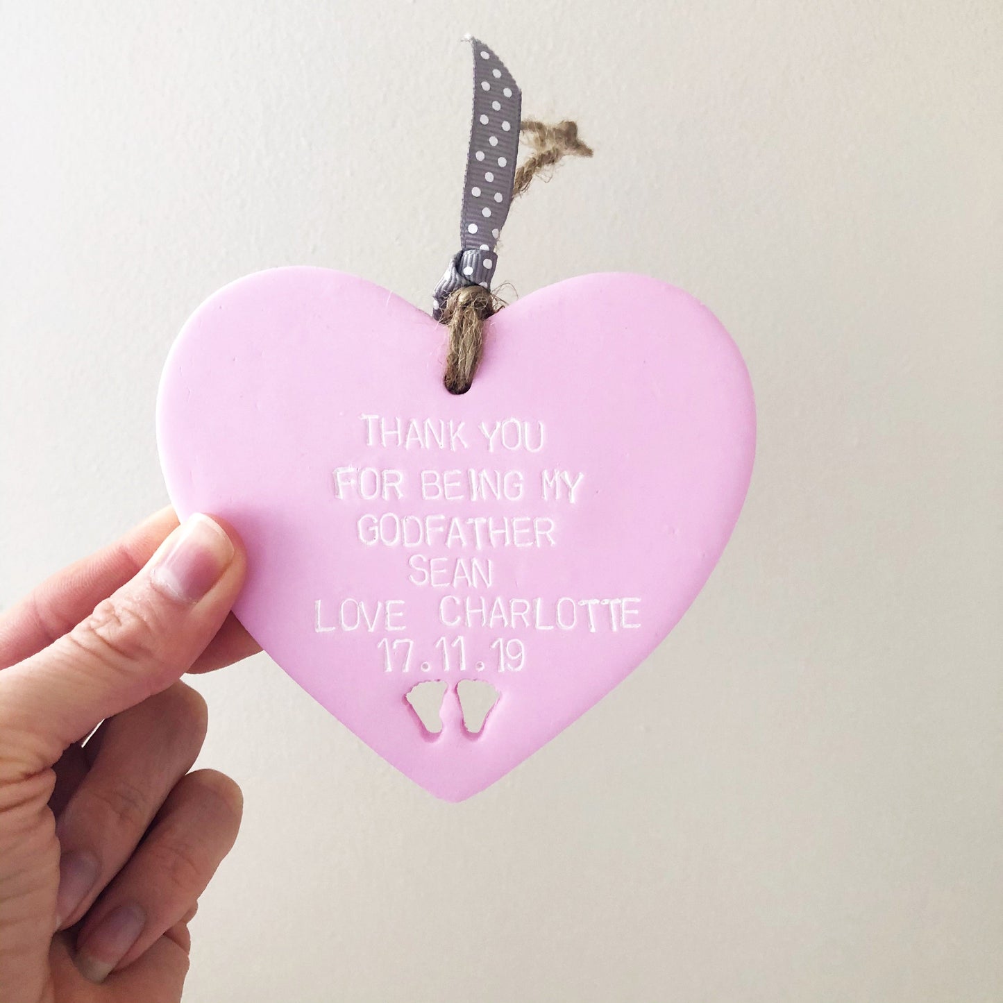 Personalised Godfather gift, pastel pink clay hanging heart with baby feet cut out of the bottom, the heart is personalised with THANK YOU FOR BEING MY GODFATHER SEAN LOVE CHARLOTTE 17.11.19