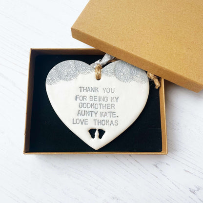 Personalised Godmother gift, pearlised white clay hanging heart with baby feet cut out of the bottom and grey lace edge at the top of the heart, the heart is personalised with THANK YOU FOR BEING MY GODMOTHER AUNTY KATE. LOVE THOMAS