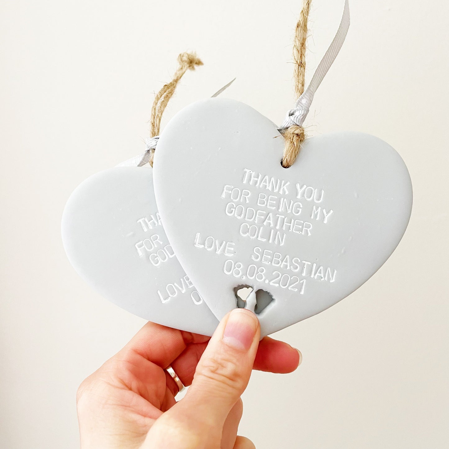 Personalised Godfather gift, 2 grey clay hanging hearts with baby feet cut out of the bottom, the heart is personalised with THANK YOU FOR BEING MY GODFATHER COLIN LOVE. SEBASTIAN 08.08.2021