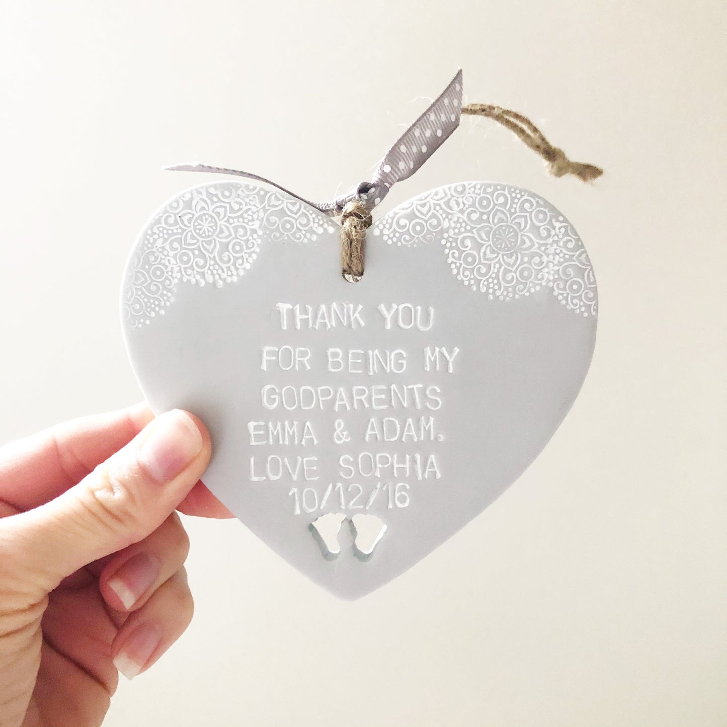 Personalised Godparent gift, grey clay hanging heart with baby feet cut out of the bottom and white lace edge at the top of the heart, the heart is personalised with THANK YOU FOR BEING MY GODPARENTS EMMA & ADAM, LOVE SOPHIA 10/12/16