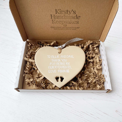 Personalised Guide parent gift, beige clay hanging heart with baby feet cut out of the bottom, the heart is personalised in white with TO ELLIE AND DAVE, THANK YOU FOR BEING MY GUIDEPARENTS, LOVE WINNIE