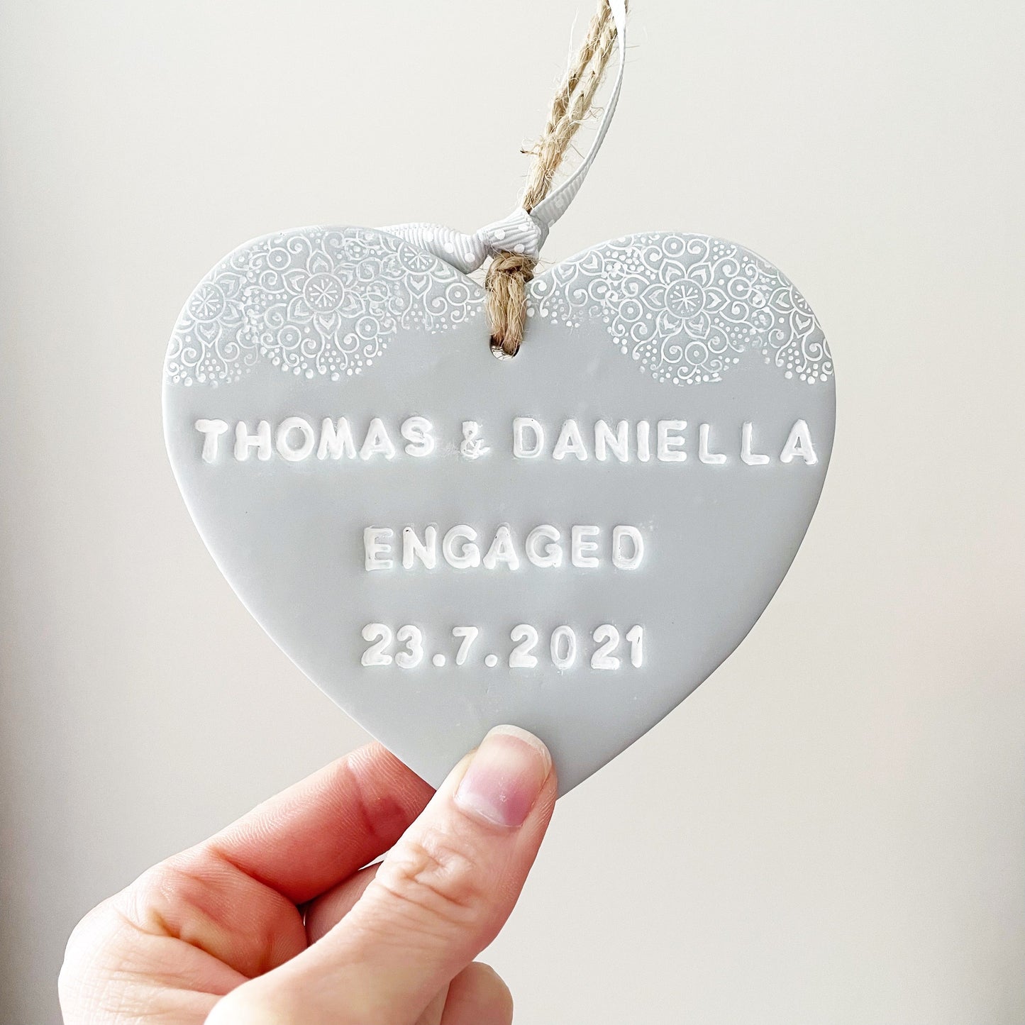 Personalised engagement gift, grey clay heart with a white lace edge at the top of the heart with jute twine for hanging, the heart is personalised with THOMAS & DANIELLA ENGAGED 23.7.2021