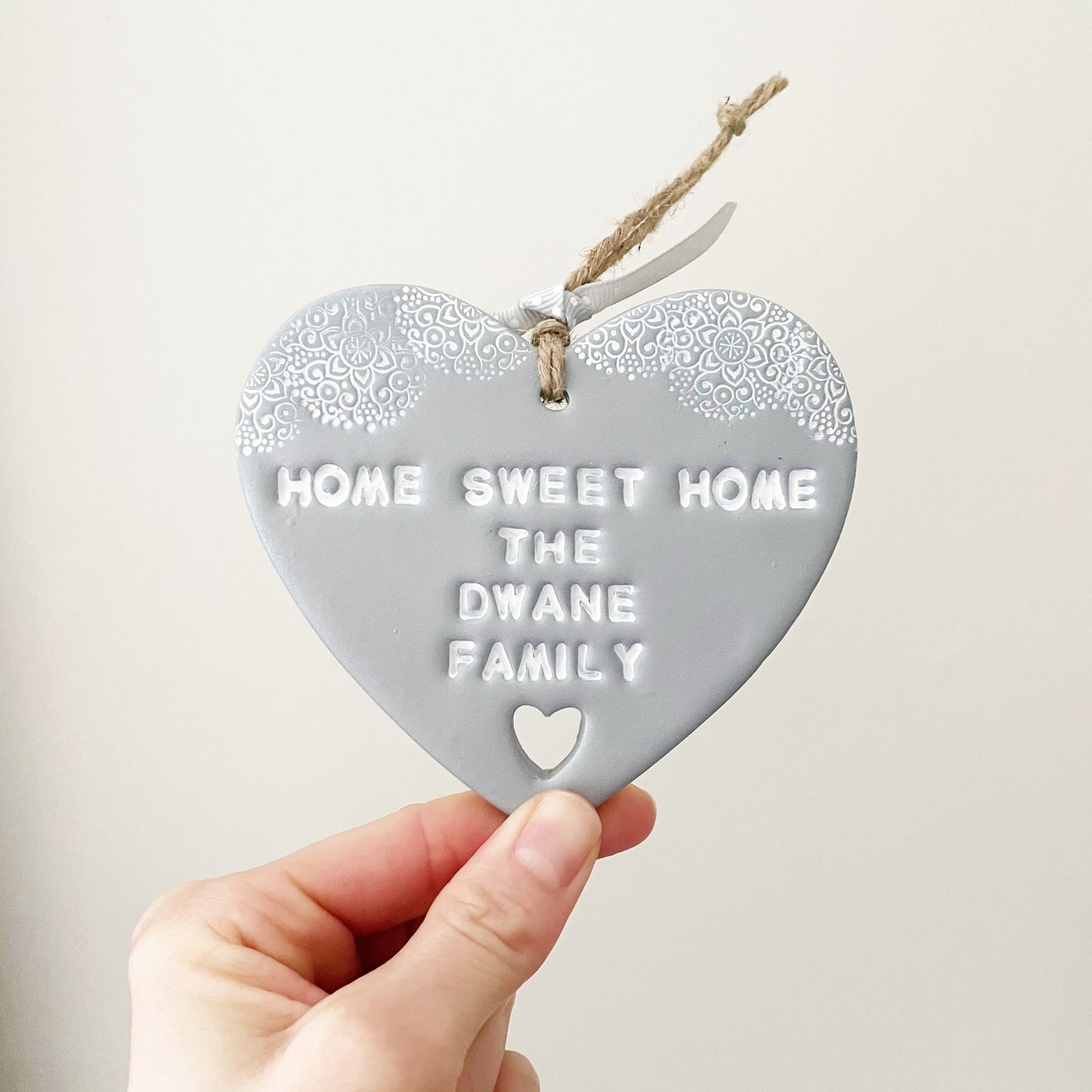 Personalised housewarming new home gift, silver clay heart with a white lace edge at the top of the heart and a heart cut out at the bottom with jute twine for hanging, the heart is personalised with HOME SWEET HOME THE DWANE FAMILY