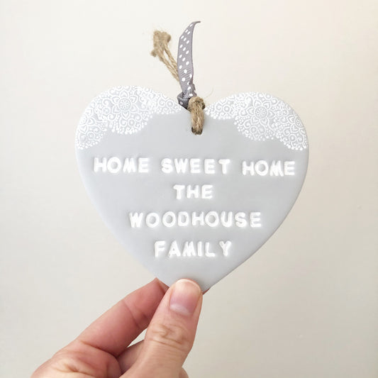 Personalised new home gift, grey clay heart with a white lace edge at the top of the heart with jute twine for hanging, the heart is personalised with HOME SWEET HOME THE WOODHOUSE FAMILY